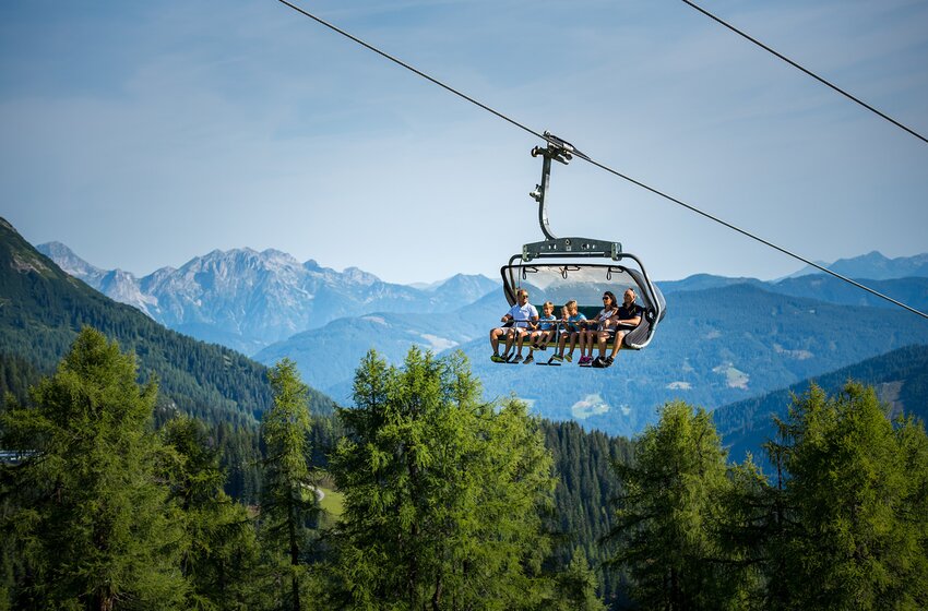 Summer uphill ride with the 6-seater Gamskogelbahn lift | © Zauchensee Liftgesellschaft Benedikt Scheffer GmbH Six people ride the 6-seater Gamskogel chairlift uphill in summer, gliding above green forest with panoramic mountain views. | © Zauchensee Liftgesellschaft Benedikt Scheffer GmbH